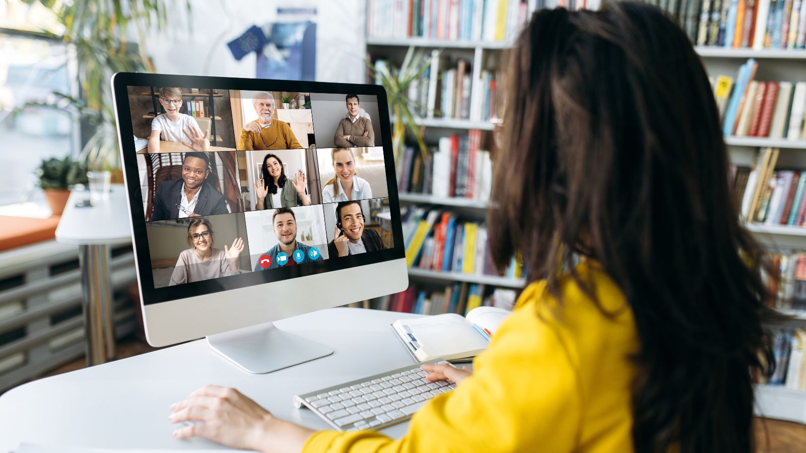 Eine Zuhörerin sitzt vor einem Bildschirm, auf dem mehrere Teilnehmende einer Online-Konferenz zu sehen sind. 