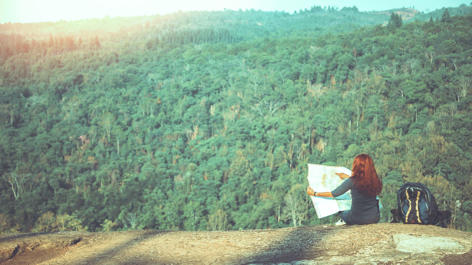 Frau sitzt vor einem Wald mit einer Karte in der Hand.