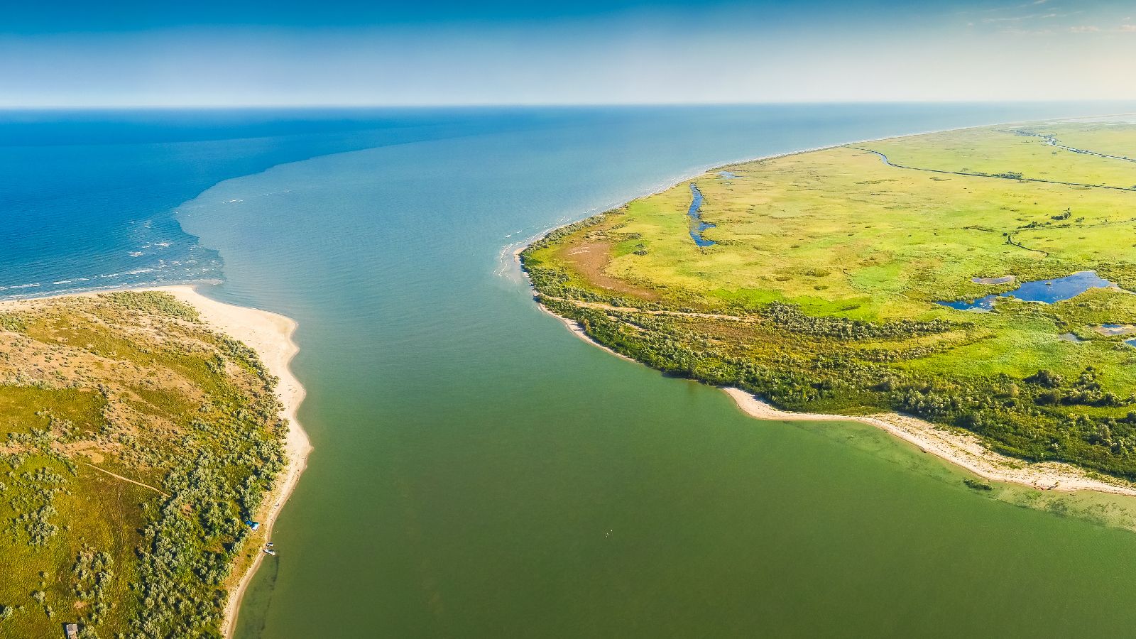 Blick aus der Vogelperspektive auf eine flache Küstenlandschaft mit grünen Wiesen und Sandstränden