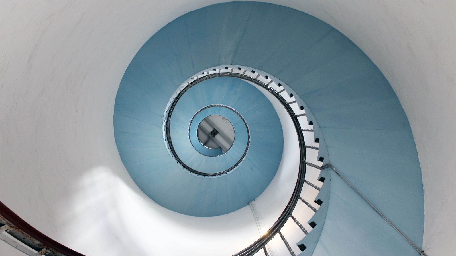Blick von unten an einer spiralförmig verlaufenden Treppe entlang, die hoch in einen Turm führt.