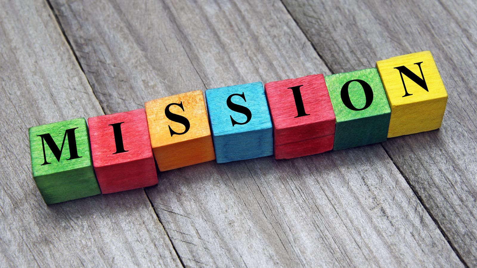 Spielklötze die auf grauem Parkett ligen und das Wort Mission bilden.