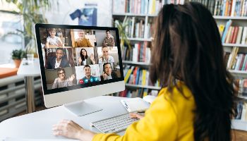 Eine Zuhörerin sitzt vor einem Bildschirm, auf dem mehrere Teilnehmer/innen einer Online-Konferenz zu sehen sind.